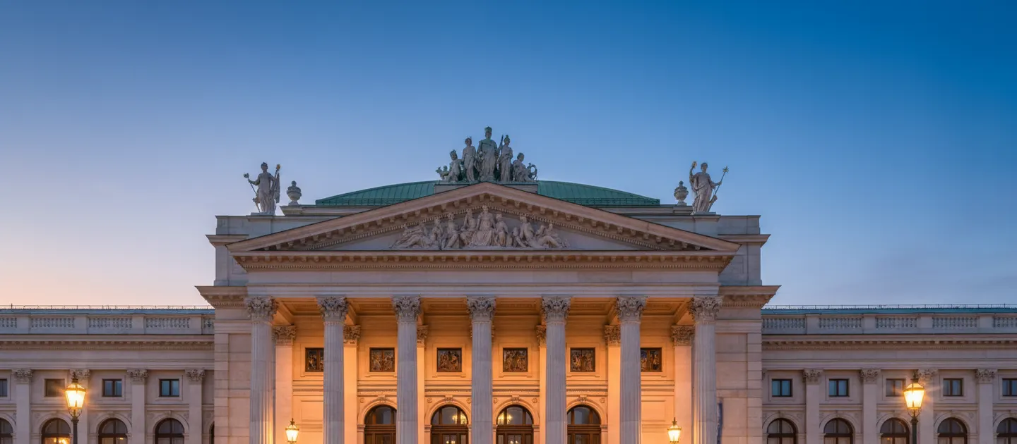 Floodlit neoclassical facade at dusk, with columns, a sculpted pediment and statues along the roofline